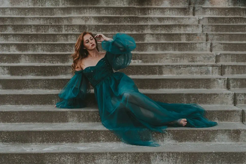 woman posing on steps in a green, flowy dress